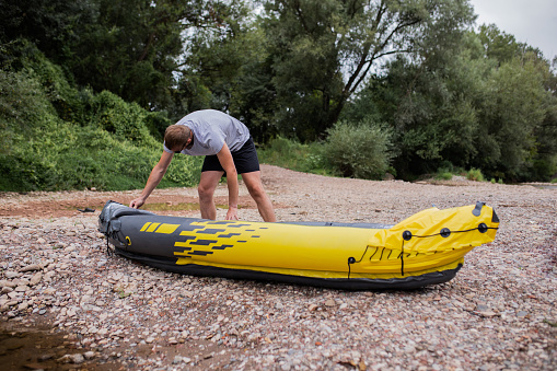 Young adventurous man, an athlete, checking if the boat is properly inflated. He is ready for kayaking.