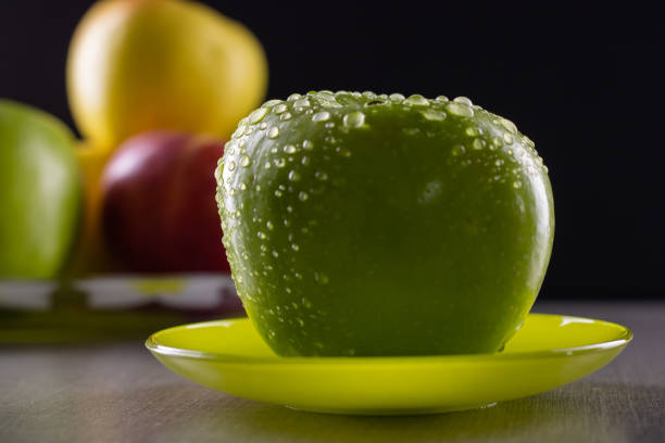 Fresh green apple on a saucer with water drops on a black background.