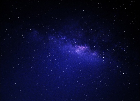 Seen from afar amidst the glittering night sky, a Milky Way photo captures an epic portrait of a cluster of stars, cosmic dust, and nebulae stretching in a gentle, luminous spiral against the dark backdrop.