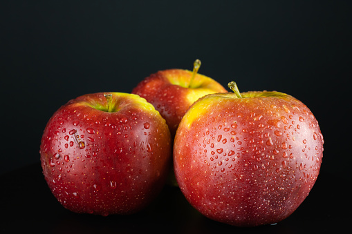 Three red ruddy apples with water droplets on a black background. Close-up vitamin.