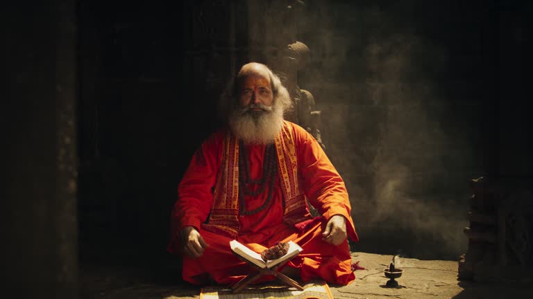 In an Ancient Temple, a Zoom in Portrait Features a Smiling Senior Hindu Monk Gazing at the Camera. Friendly Old Indian Man Poses, Seeking Guidance and Wisdom from His Religious Sacred Book