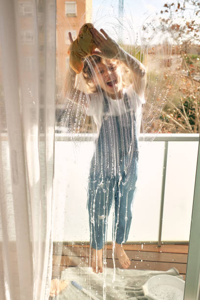 istock Cheerful boy washing windows with rag at home 1616945064