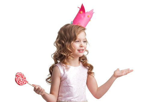 Happy laughing princess girl in crown and pink dress with lollipop on white background