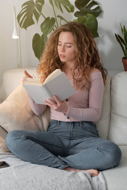 istock Young woman reading book on sofa 1616958174