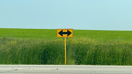 Street Sign with a double arrow on Highway with corn field farm.