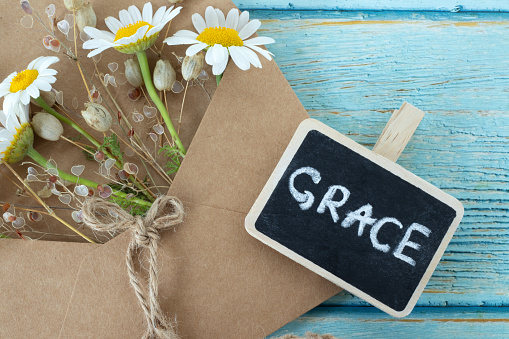 Grace, handwritten text with chalk on small blackboard, vintage paper and flowers on wooden table. Top view. Christian biblical concept of mercy, love, and salvation of God Jesus Christ.