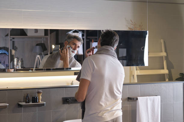 istock Adult male looking at mirror and shaving using razor 1617003141