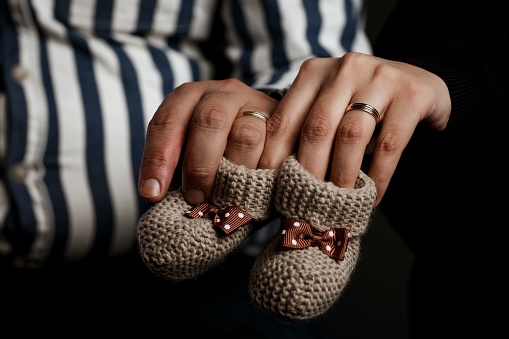 An intimate shot of a loving couple's hands cradling a pair of tiny, grey and white striped newborn baby socks