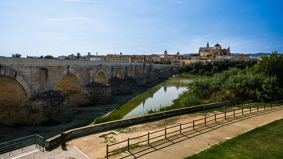 A 16x9 horizontal landscape photograph showcasing the majestic Mezquita-Cathedral and the historic Roman Bridge in Córdoba, taken with a wide-angle lens. Captured during daylight hours with clear skies, this image emphasizes the grandeur and architectural heritage of Córdoba.