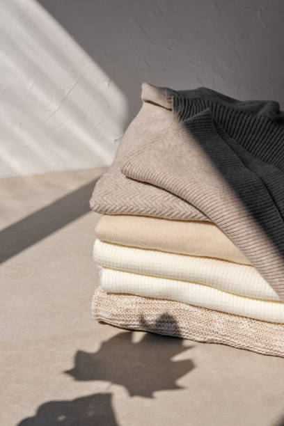 istock Stack of beige, taupe, white, light brown knitted sweaters on neutral beige background with aesthetic lifestyle sunlight shadows. Fall leaf in silhouette. Aesthetic lifestyle autumn clothes concept 1617055047