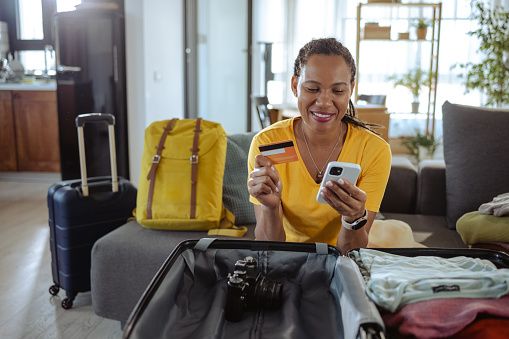 Mature African American woman packing for a trip and using online payment services