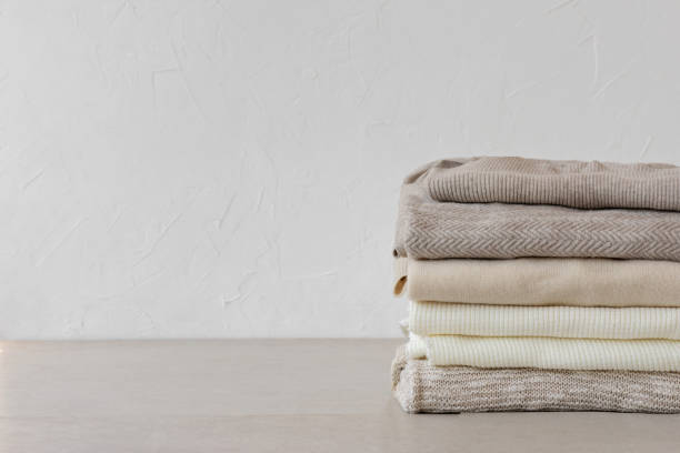 istock Wool knitted clothes stack closeup in neutral beige colors on table on white empty wall background. Aesthetic fashion minimalist wardrobe concept, warm autumn knitwear jersey 1617059629
