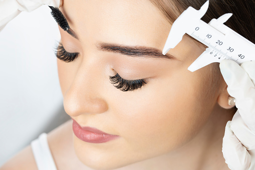 Young woman in profile with eyes closed undergoing treatment to laminate and iron her eyebrow.