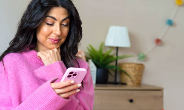 istock Woman smiling and using her phone at home 1617108818