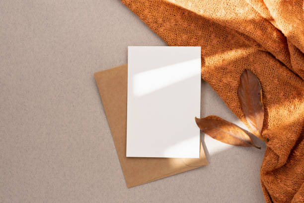 istock Blank paper card mock up, envelope, brown fall leaves, orange knitted textile on neutral beige background with aesthetic sun light shadow. Autumn business branding template, wedding invitation design 1617115147