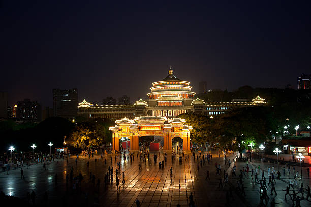 Unrecognizable people dancing on Chongqing's People's Square with illuminated Great Hall of People in the background. The Great Hall is inspired from Beijing's Temple of Heaven.
