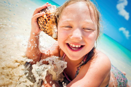 Adorable little girl at tropical beach applying sunblock cream