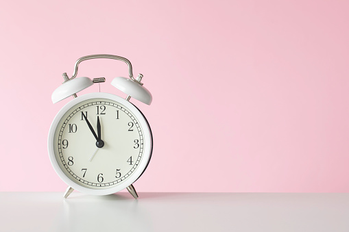 Retro style alarm clock on pink background.