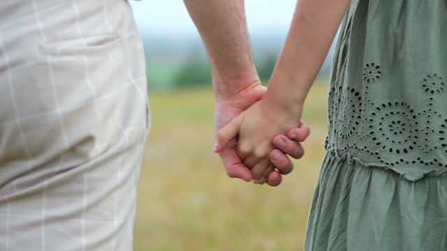 Couple of man and woman walk hand in hand across field