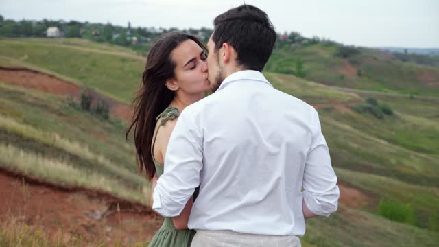 Man and woman kiss on hilly plain enjoying view of village