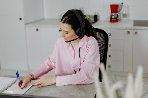 Displaying dedication to her role, a young woman operates as a call center professional, utilizing a laptop and headphones to provide efficient customer service from her home office