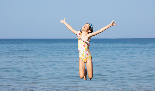 Little cute happy girl jumping into the sea on the shore on a summer day