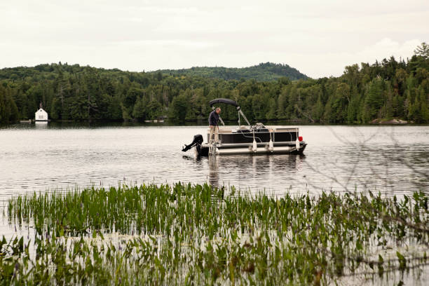 Senior man standing on a pontoon boat on a lake in summer. He is in his sixties and is wearing casual clothes. Horizontal outdoors full length shot with copy space. This as taken in the Laurentides, Quebec, Canada.
