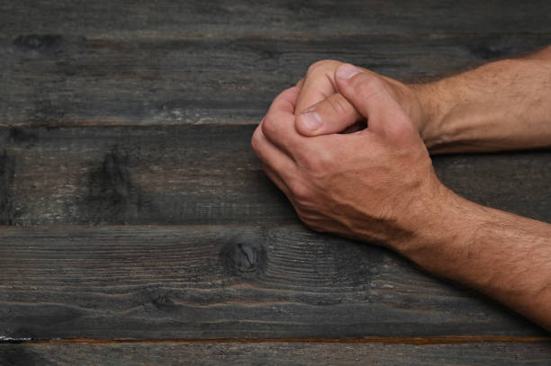 The man's hands are folded on a wooden table. concept. Participation in negotiations, interviews, meetings. At an appointment with an employer or supervisor. Without a face. Unrecognizable. Close-up