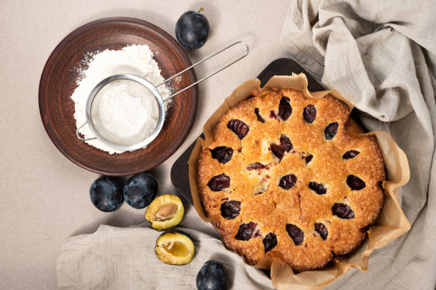 istock Plum pie baking. Cake with plums, cinnamon, sugar powder on plate, on neutral beige linen tablecloth 1617187525