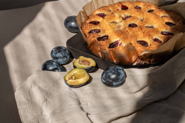 istock Homemade plum pie and plums on beige tablecloth with sunlight shadows. Sweet rustic bakery, traditional baked fruit cake, torte 1617191301