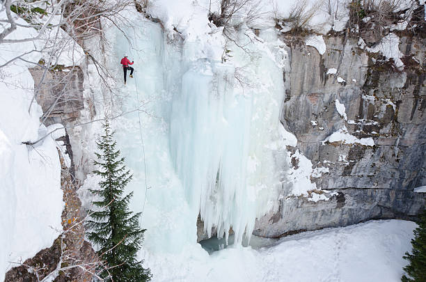 Ice Climbing Steep Frozen Waterfall in Winter.  Man leads up steep ice gully using ice axes and climbing rope in large natural amphitheater.  Captured as a 14-bit Raw file. Edited in ProPhoto RGB color space.