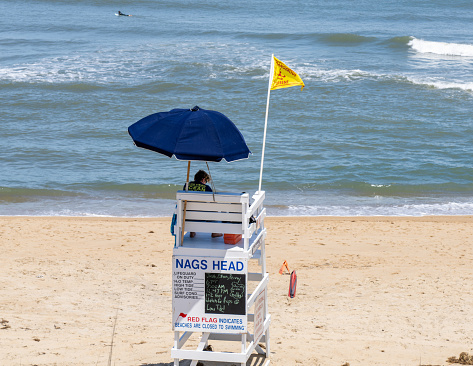 Nags Head North Carolina - May 28 2023: A Lifeguard Sitting in a Stand in Nags Head Watching the Water with a Dangerous Current Flag Flying for Rip Currents