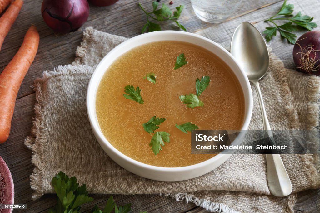 Chicken bone broth or soup with herbs and vegetables Chicken bone broth with parsley and vegetables in a white soup bowl on a table Bone Broth Stock Photo