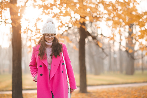 Happy stylish woman wear pink autumn jacket and knitted hat walk on city street outdoor. Fall season.
