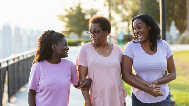Three generations of African-American women walk in park A multi-generation African-American family having fun walking together in a park on a city waterfront. The three generations of women are smiling, holding hands. The senior grandmother is in the middle between her teenage granddaughter and her adult daughter. teenage girl with grandmother stock pictures, royalty-free photos & images