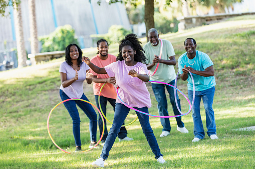 A three generation African-American family having fun together outdoors spinning plastic hoops around their waists. The 14 year old granddaughter is the center of attention.