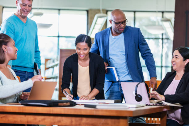 istock Adult students gather at table in library to study 1617252135