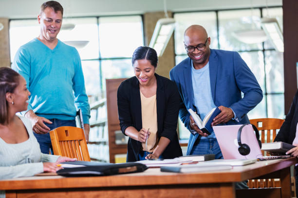 istock Adult students gather at table in library to study 1617252137