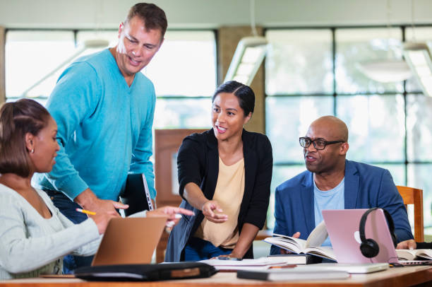 istock Adult students gather at table in library to study 1617252139