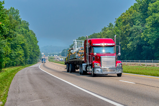 Horizontal shot of a flatbed eighteen wheeler transporting building materials on an interstate highway.