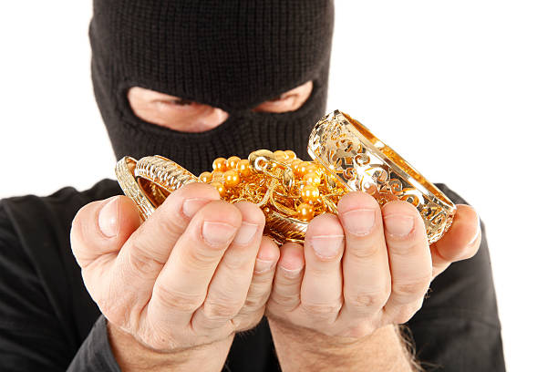 Burglar in black mask holds stolen golden loot in hands stock photo