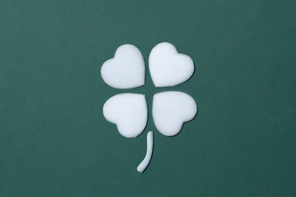 Simple art flatlay of a four leaf clover or cloverleaf made with a white heart on a forrest green background. Saint Patrick Ireland good luck thematic.