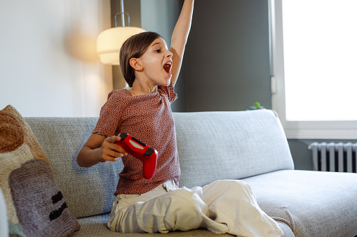 A playful teenage girl is holding a game controller and celebrating victory in a video game