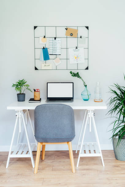 istock Modern Contemporary workplace design. White desk with laptop mockup empty screen, grid mood board with pinned notes and plans, green plants, office supplies at work space in home office room interior. 1617315882