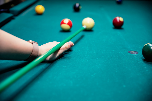 Young female hit the ball in billiard pool with colorful balls.  Woman playing billiards in the dark billiard club. Close-up