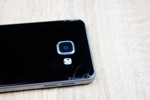 Cracked smartphone from the back. Fall damage to smartphone. Broken smartphone.