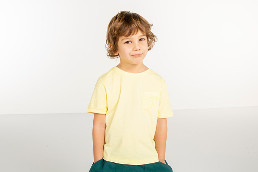 Portrait of cute little boy. 5 year old boy make face on white background. Yellow t-shirt . White people.