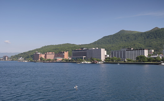 Toyako-cho, Japan - June 8, 2023: Large resort hotels line the waterfront promenade of Lake Toya, a caldera lake. Spring afternoon in the volcanic landscape of Shikotsu-Toya National Park.