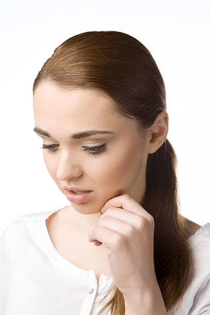 Thoughtful young woman holding her hand at chin, staring down stock photo