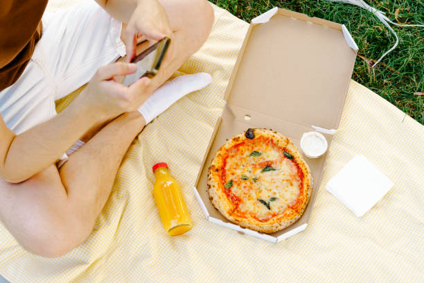 istock A young man scrolls through the phone while sitting on a yellow mat with a pizza in a box and orange juice. The concept of a remote food delivery service 1617538202